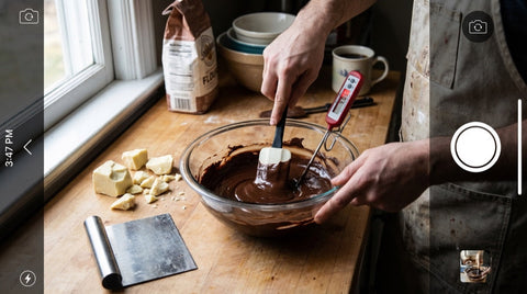 Tempering dark chocolate on a kitchen counter with candy thermometer and cocoa butter pieces