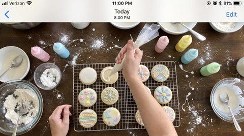 Piping royal icing onto decorated sugar cookies on a kitchen table